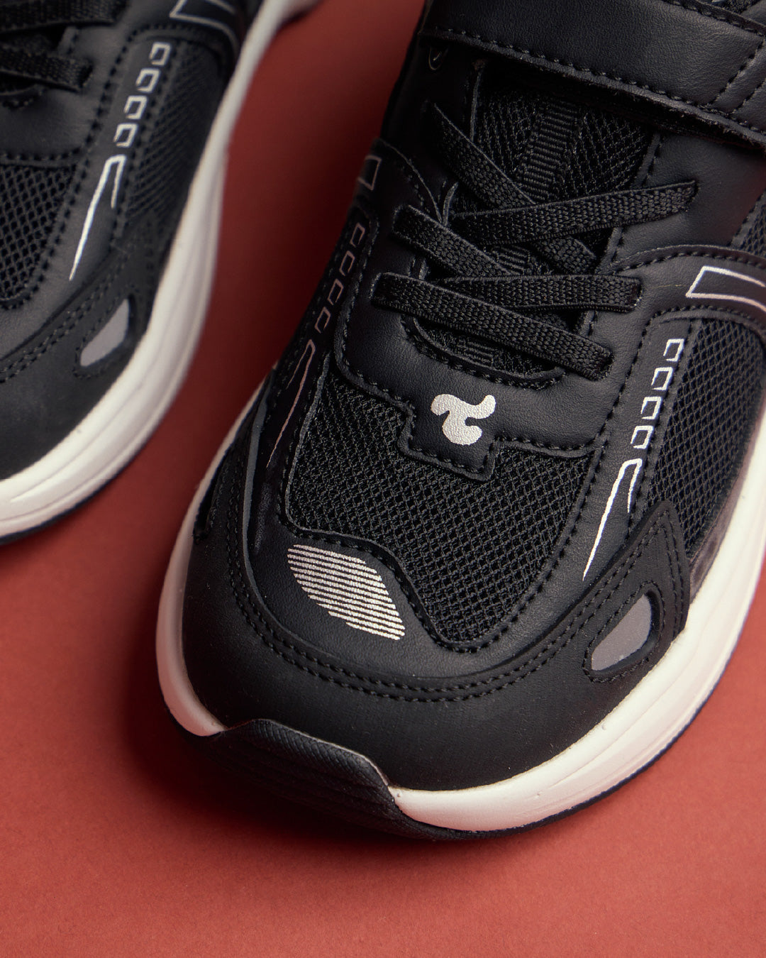Play Junior in Black, close-up from the front showing the foot-shaped front, reflective side detail and level outsole.