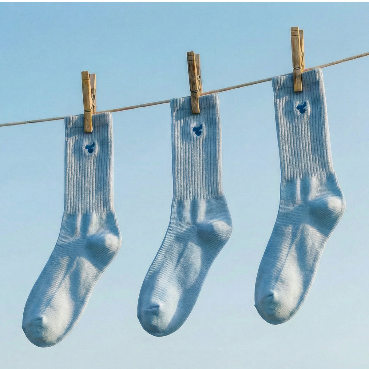Three pairs of Tiny Socks in Soft Marina hanging on a clothesline.