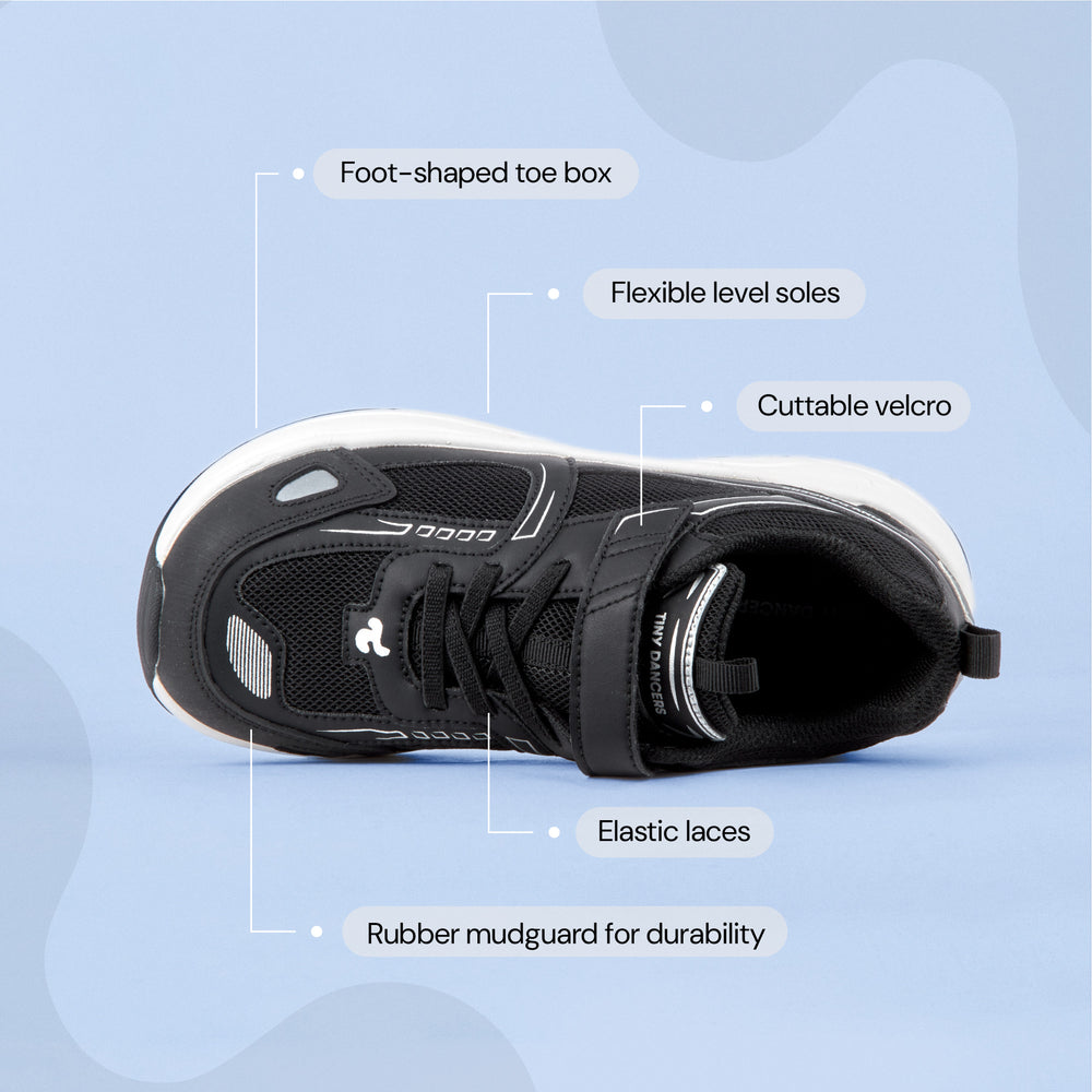 Play Junior in black from above, labelled: foot-shaped toe box, flexible level soles, cuttable velcro, elastic laces, rubber mudguard.