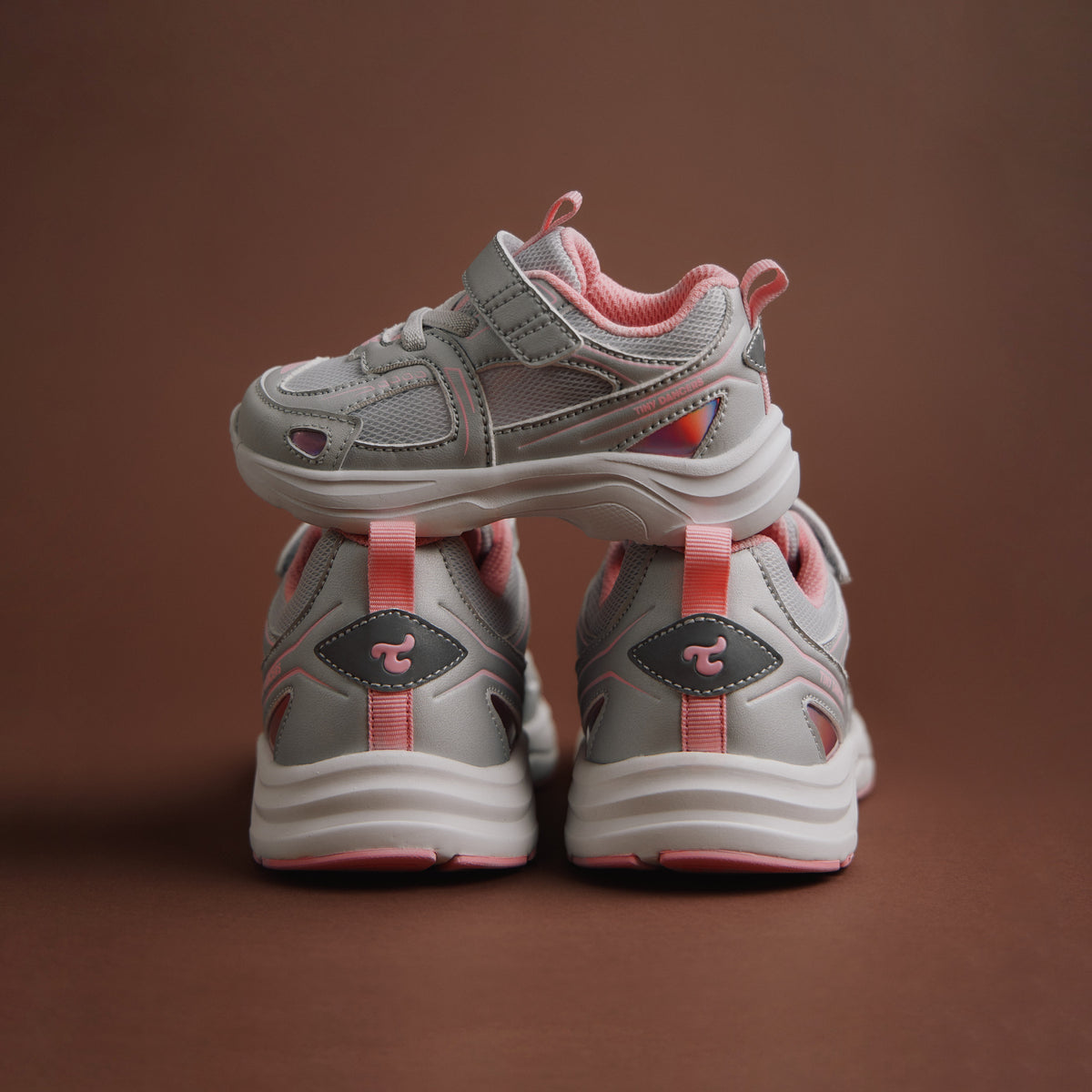 A pair of Play Infant in silver pink, rear view with logo patch on a warm brown background.