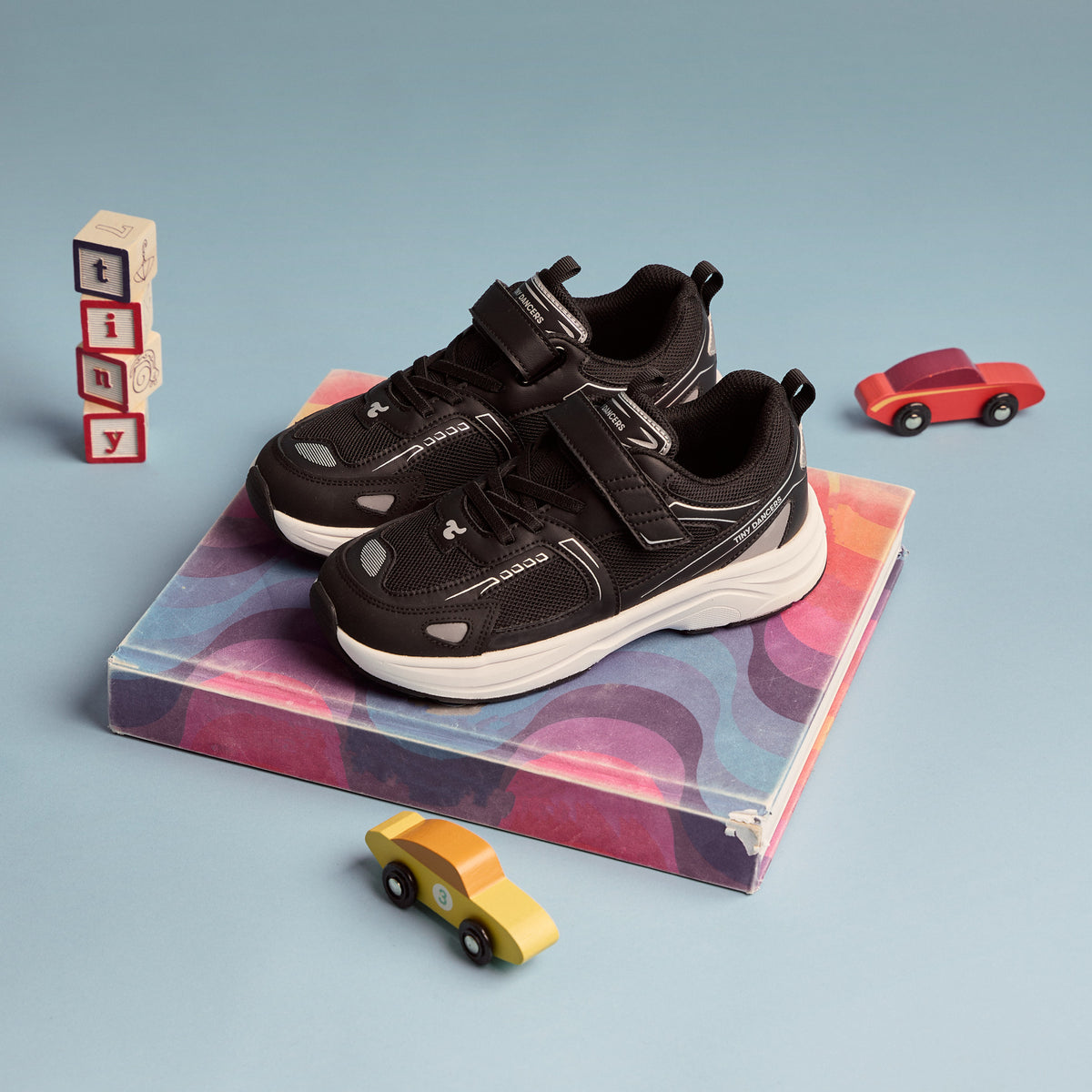 A pair of Play Junior in black on a marbled plinth with wooden tiny blocks and toy cars.