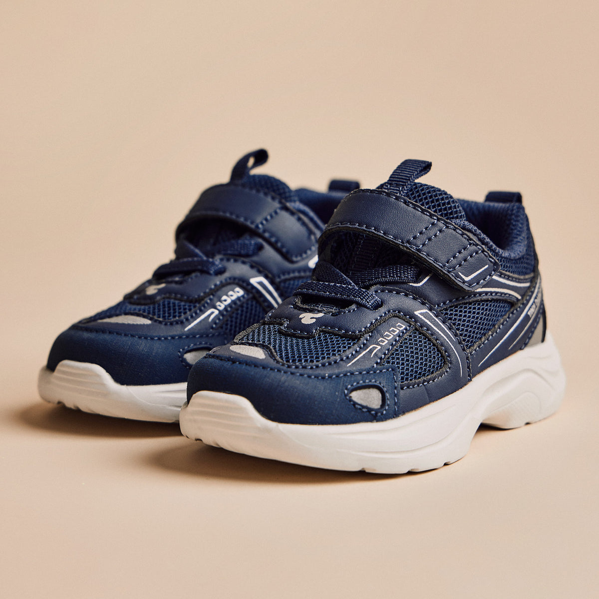 A pair of Play Infant in navy, three-quarter view on a warm beige background.