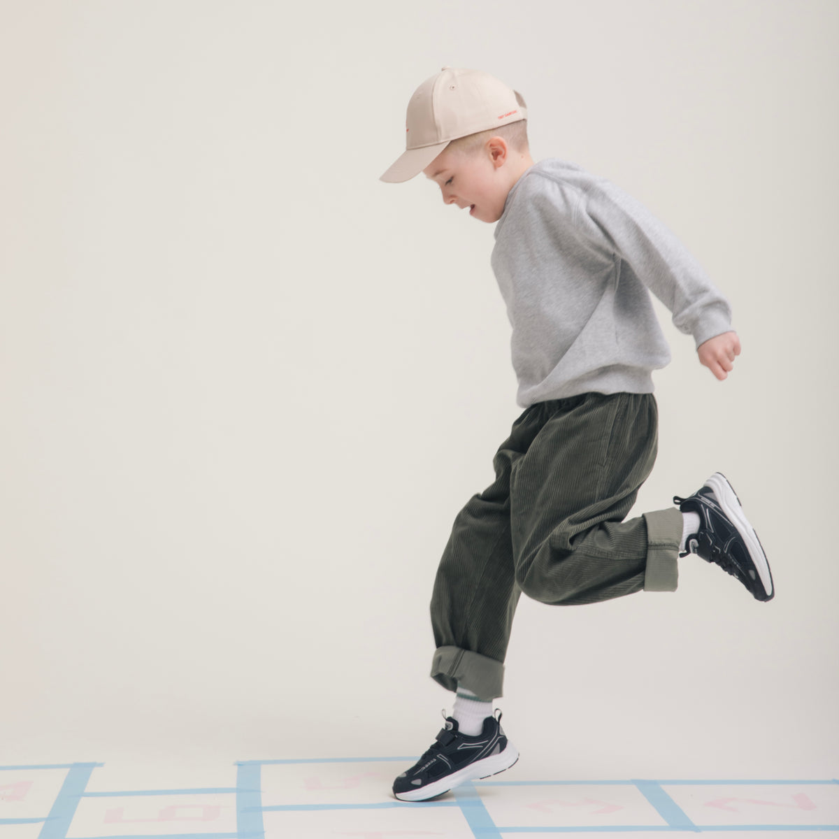 Child mid-hop across a hopscotch grid in Play Junior black.