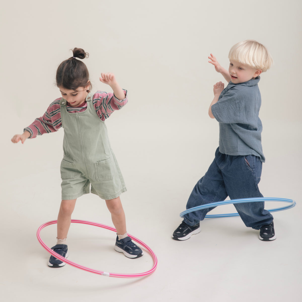 Two children dancing with hula hoops in Play Junior navy, studio setting.