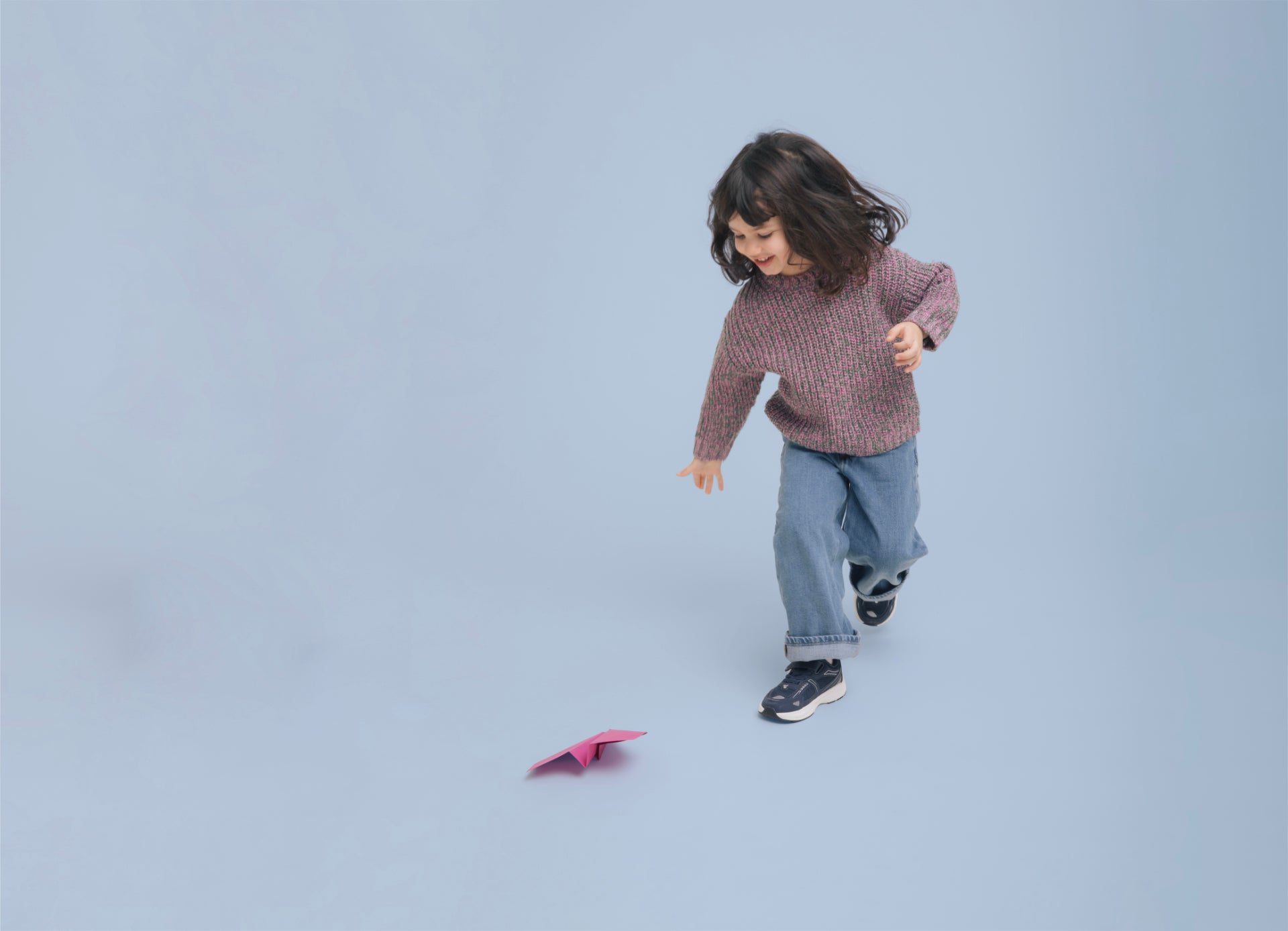 A child walking in Play Junior navy with a paper airplane on the ground.
