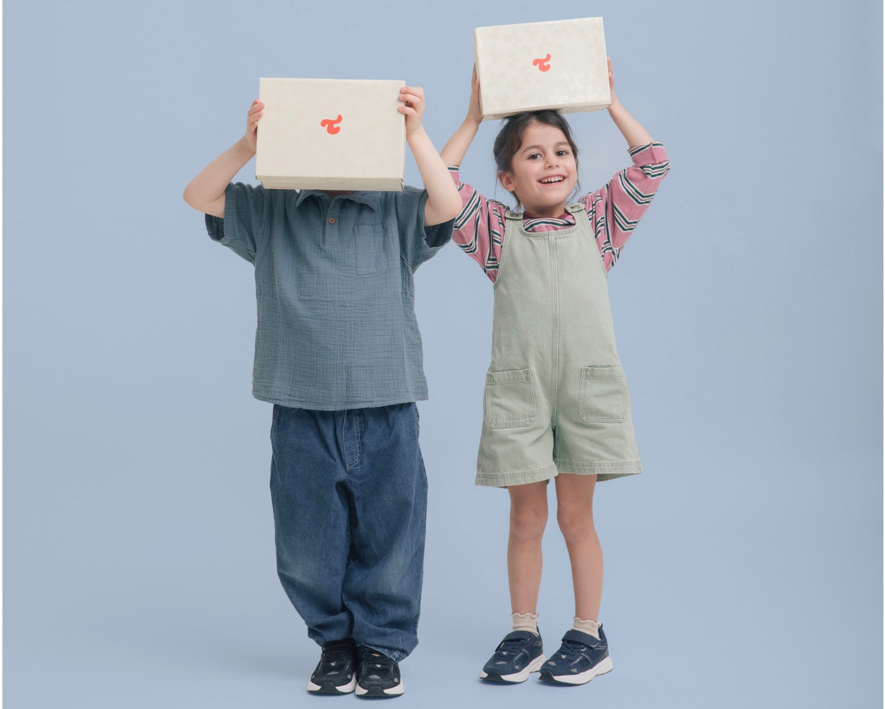 Two children holding Tiny Dancers shoe boxes above their heads, on a blue studio background.