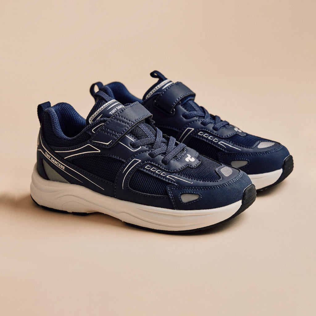 A pair of Play Junior in navy, three-quarter view on a warm beige background.
