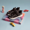 A pair of Play Junior in black on a marbled plinth with wooden tiny blocks and toy cars.