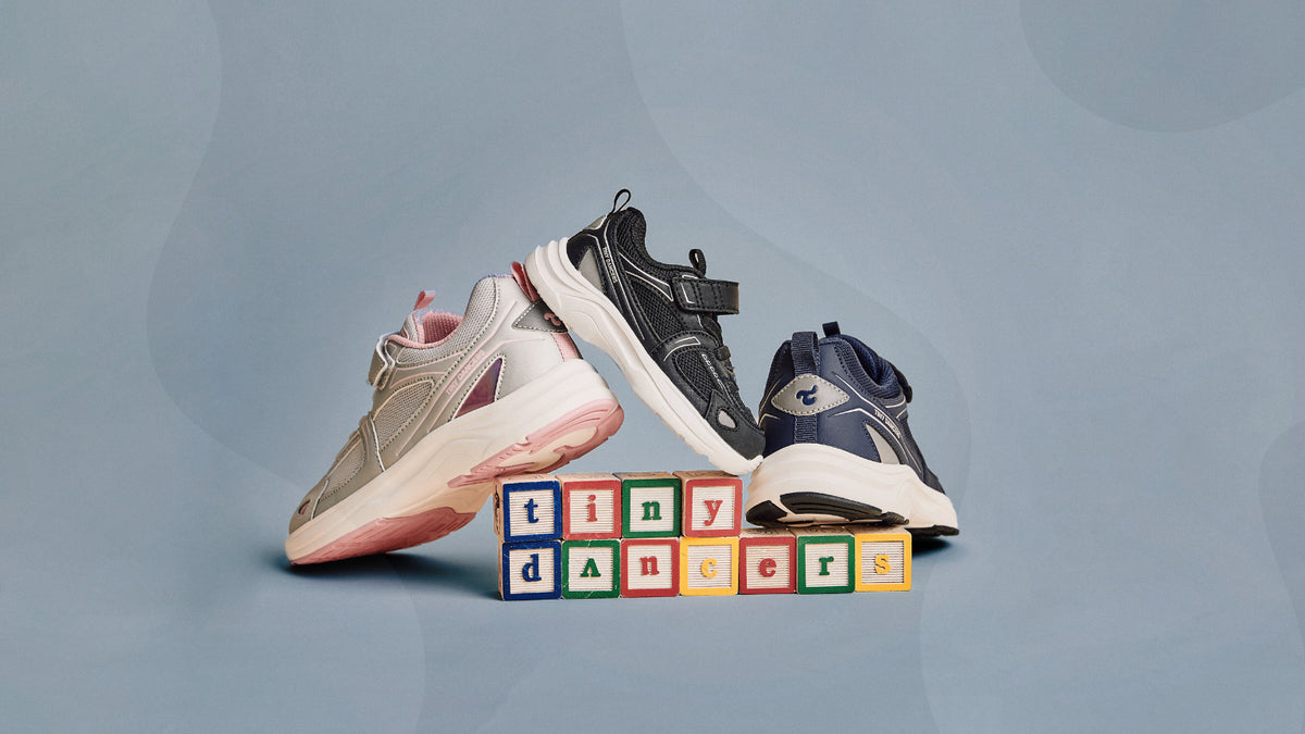 Three pairs of Play shoes — Silver Pink, Black and Navy — arranged around wooden alphabet blocks spelling "tiny dancers" on a blue background.