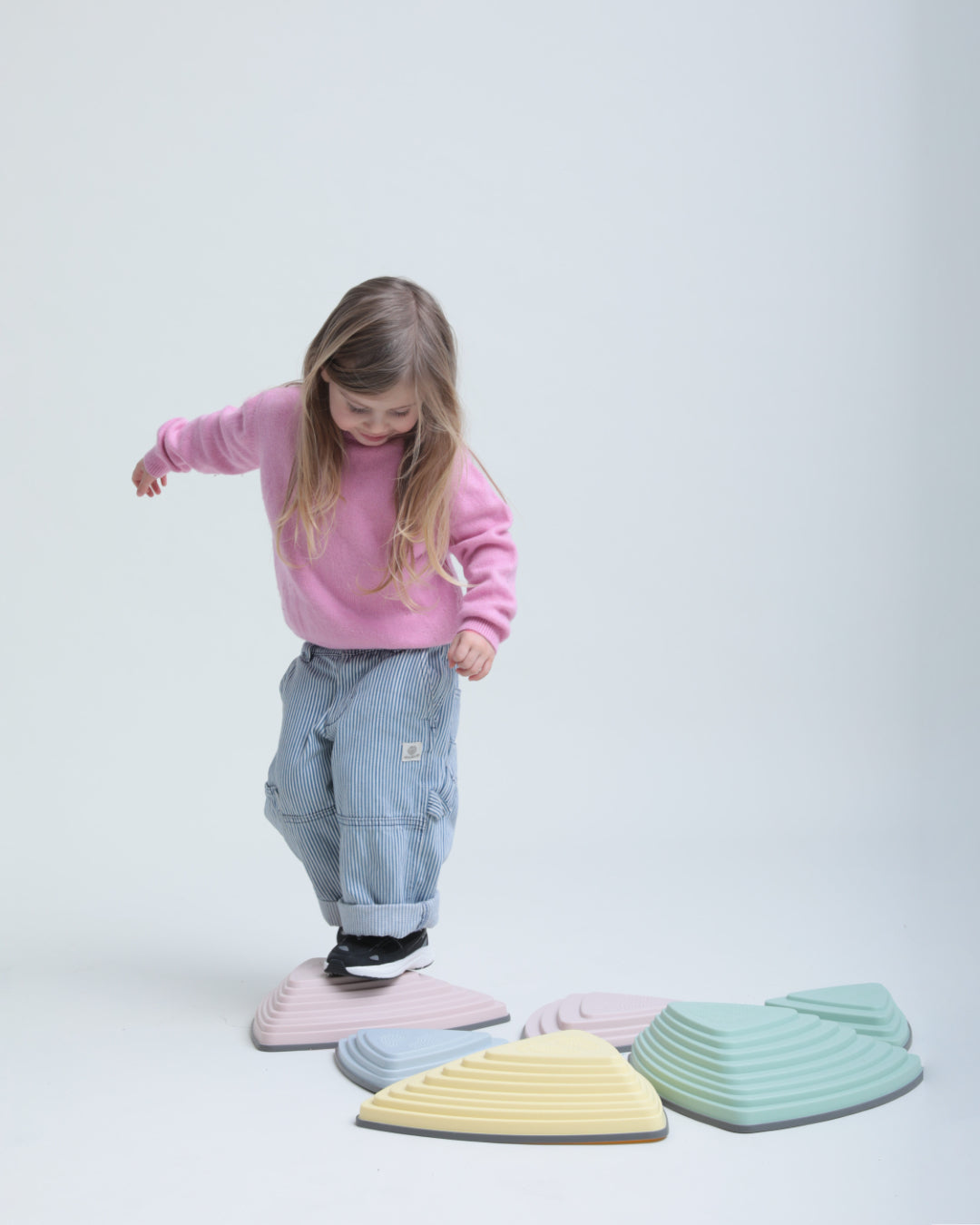 Child stepping across pastel balance stones in Play Junior black.