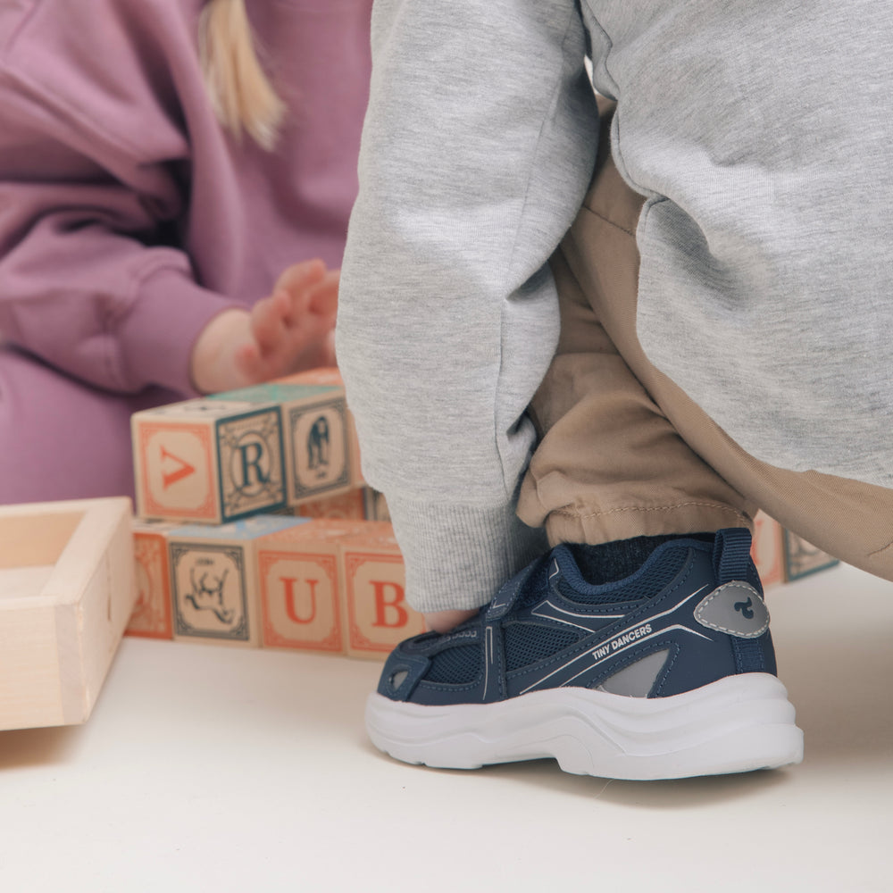Child sitting with wooden alphabet blocks, wearing Play Infant navy.