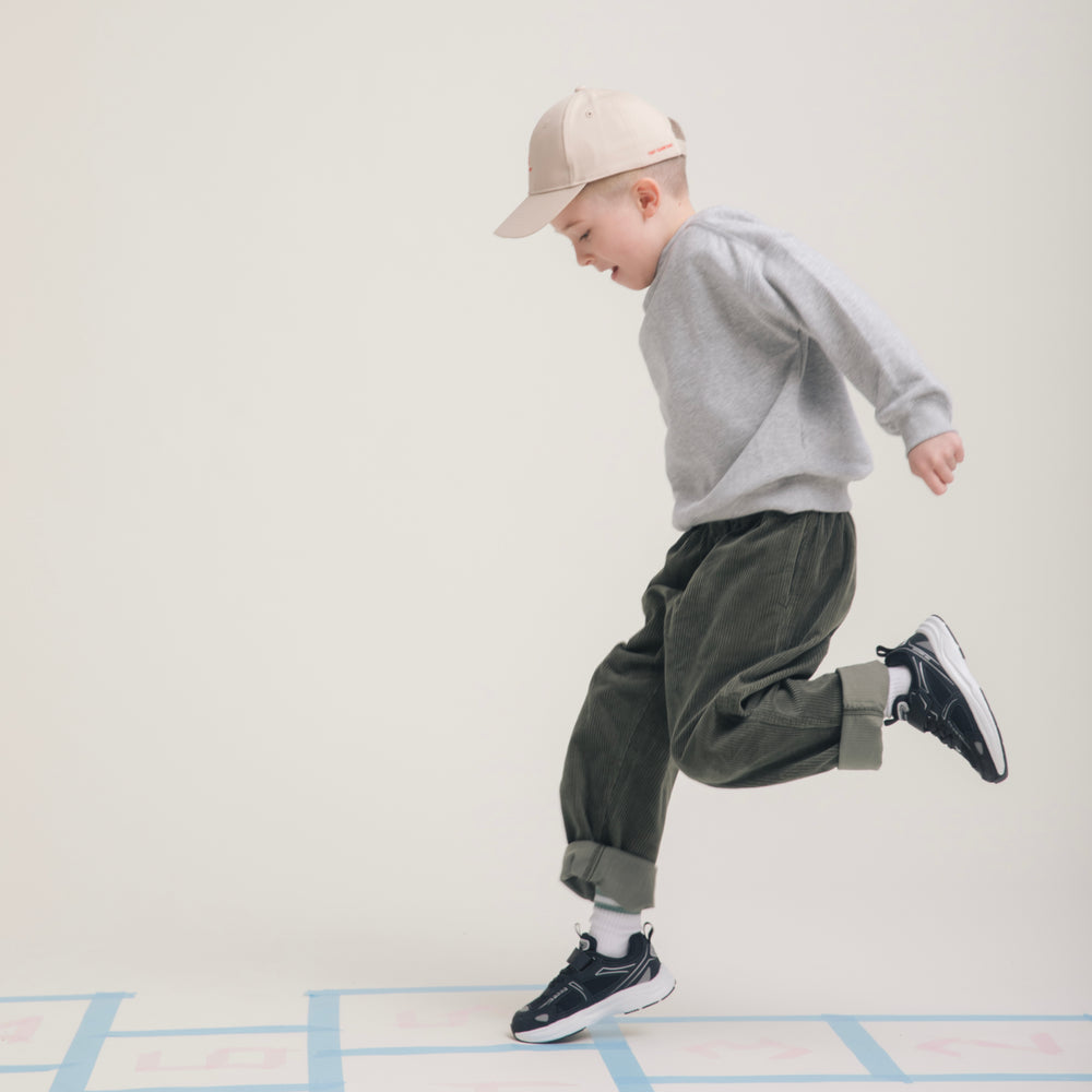 Child mid-hop across a hopscotch grid in Play Junior black.