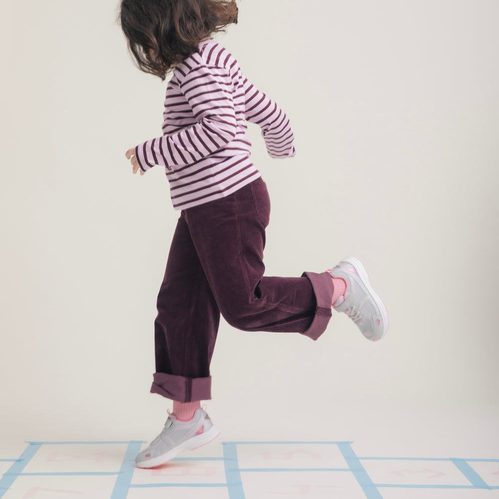 Child mid-hop across a hopscotch grid in Play Junior silver pink.